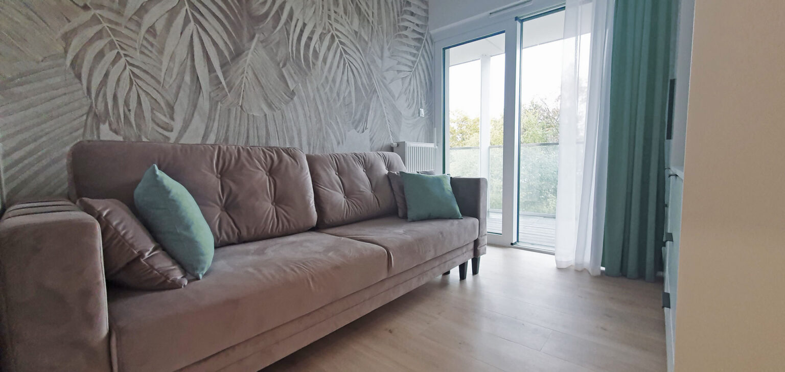 Pokój gościnny z widokiem na morze, welurowa sofa rozkładana w odcieniach beżu