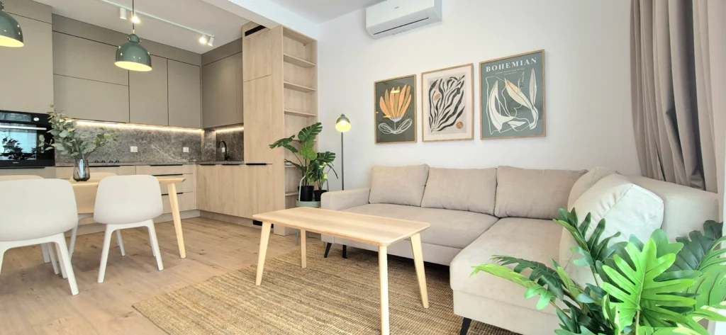 Kuchnia otwarta na salon z narożną sofą i botanicznymi plakatami – mieszkanie na wynajem